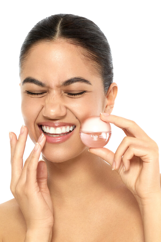 Beautyfotografie, Model lächelt und hat ein rosa Lipbalm in der Hand.