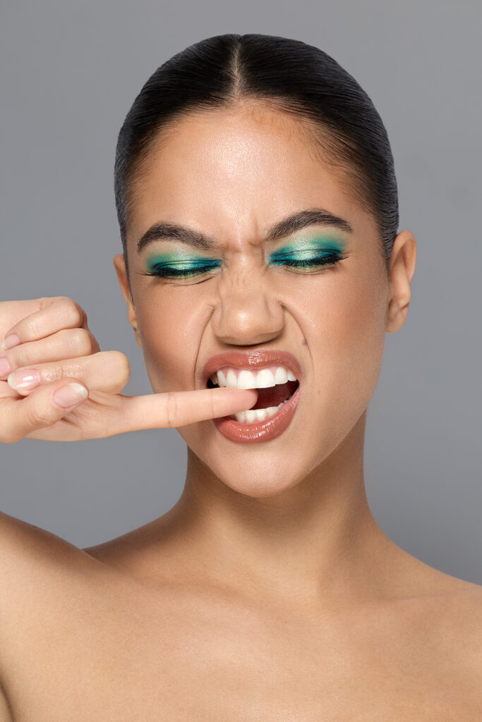 Beautyfoto, starkes Makeup, Model hat ein grünes Augenmakeup und beisst sich auf dem Finger